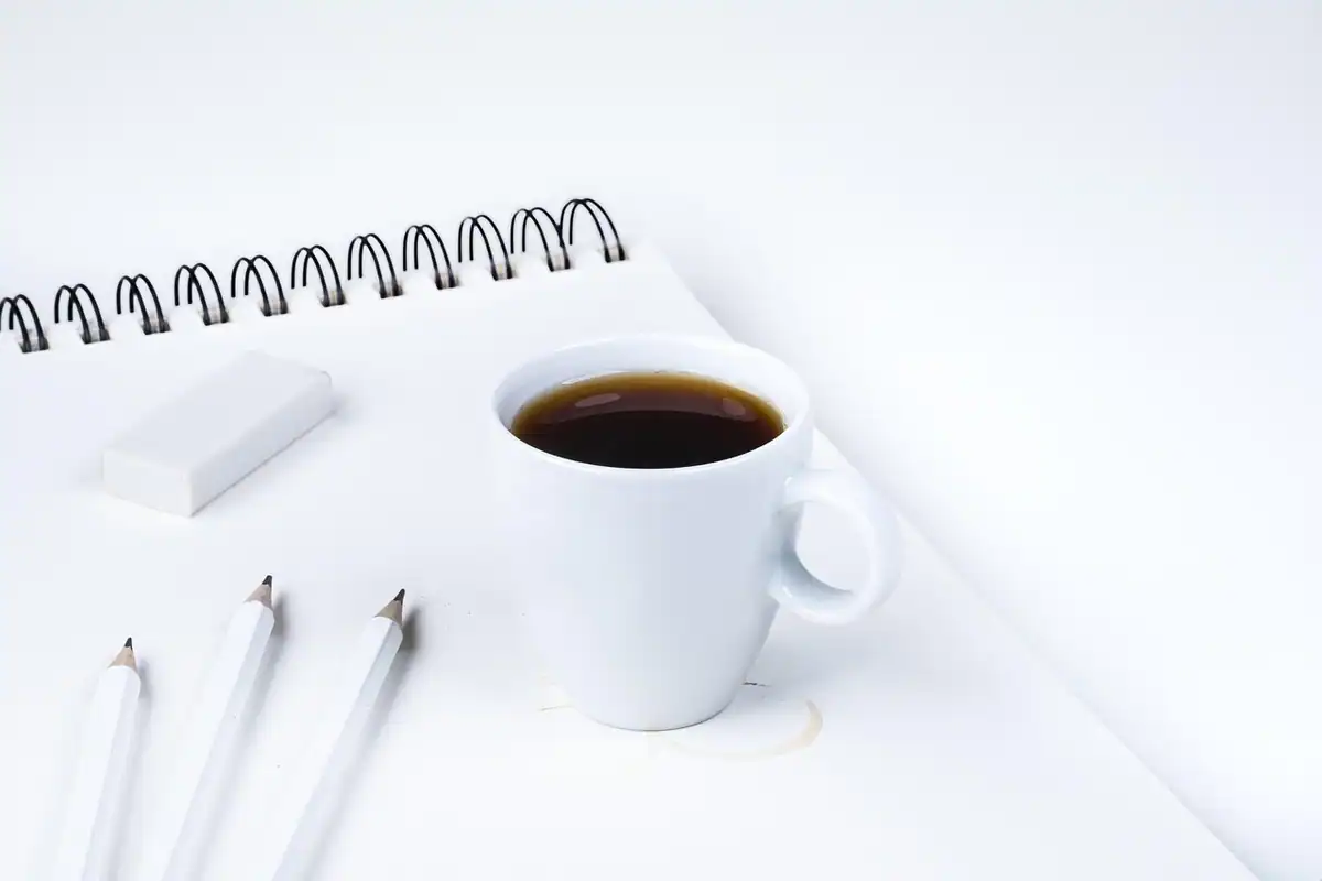 Creioane colorate și o gumă de șters așezate pe un birou, lângă o cană de cafea
