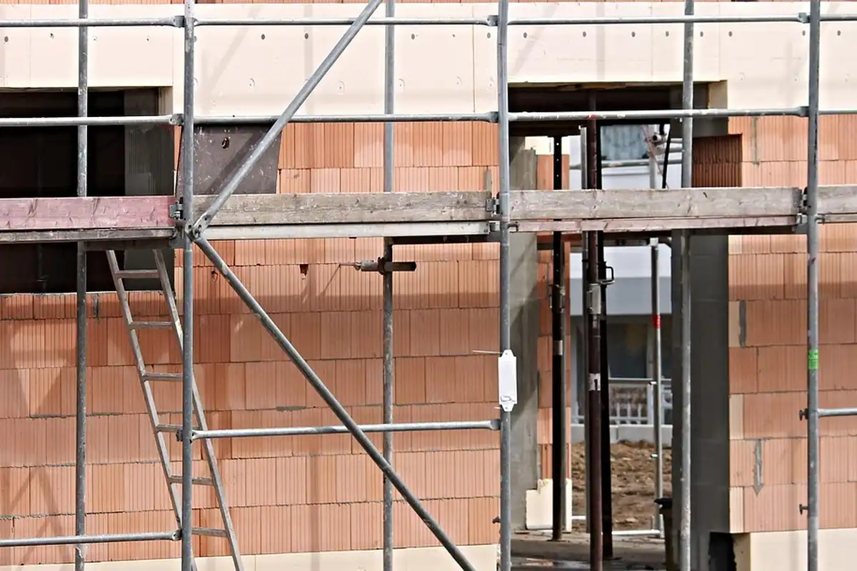 Casă în construcție, cu pereți de piatră, goluri pentru ferestre și schele din lemn, pe un șantier