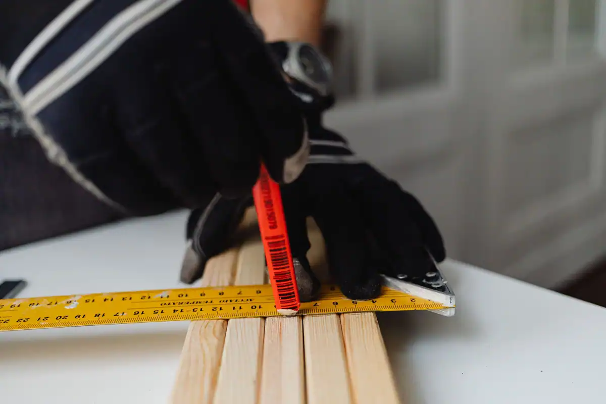 Mână în mănușă măsoară cu ruleta galbenă o grindă de lemn