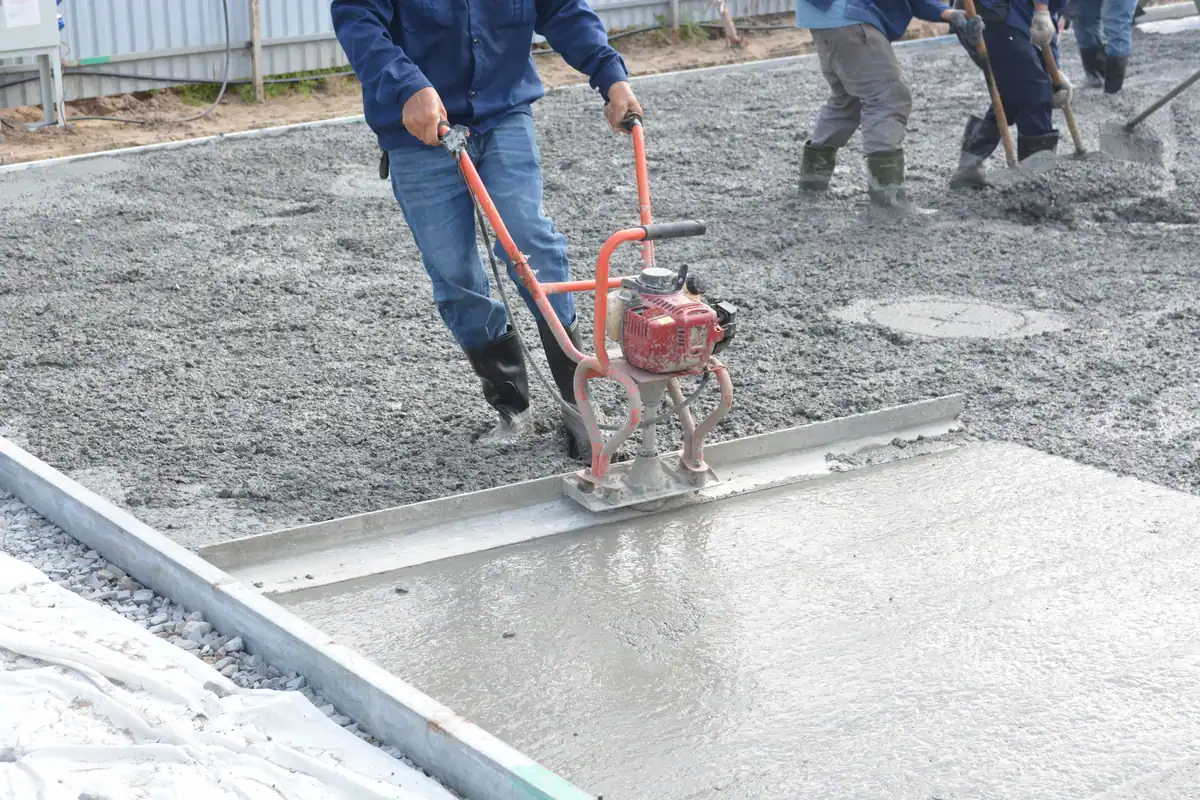 Muncitori nivelează cu o mașină vibrantă o placă de beton turnată pe pietriș