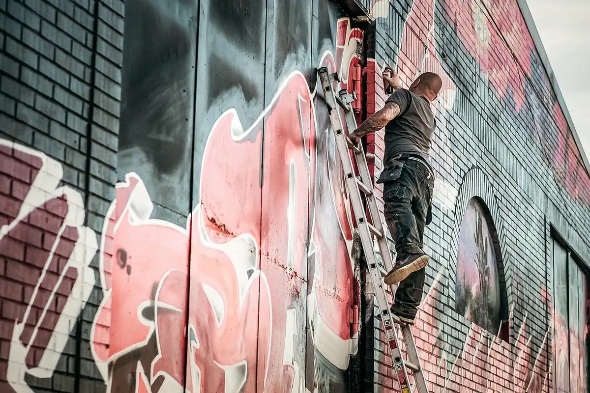 Artist de graffiti care lucrează cu spray pe un zid de cărămidă, lângă o scară