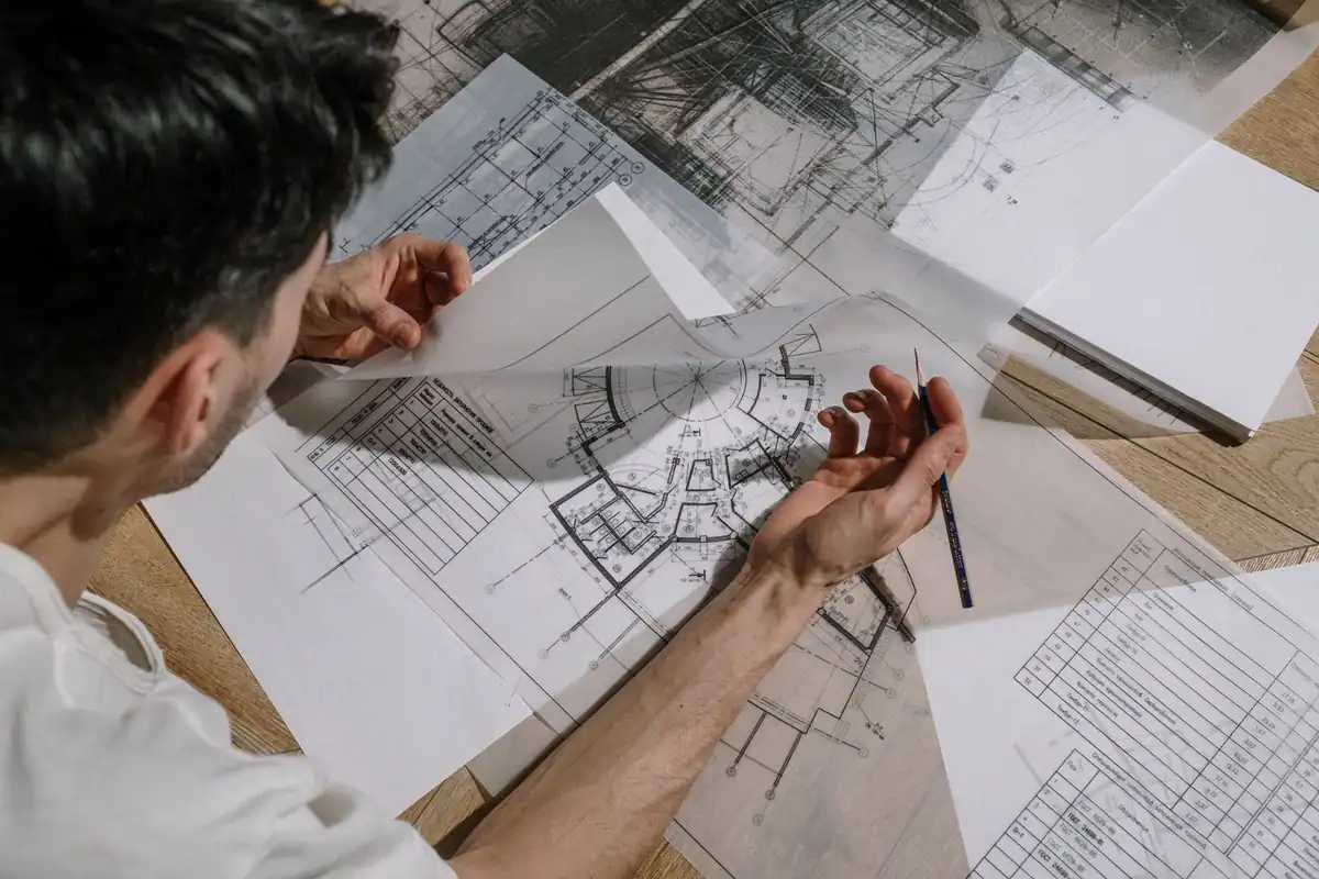Arhitect care studiază și schițează pe planuri de arhitectură detaliate, într-un birou