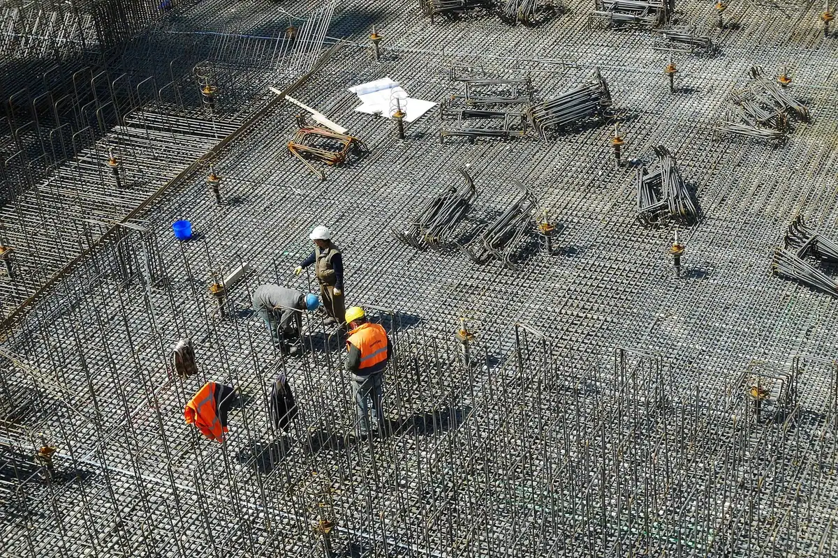 Muncitori în veste portocalii verifică armătura unei fundații, văzută de sus