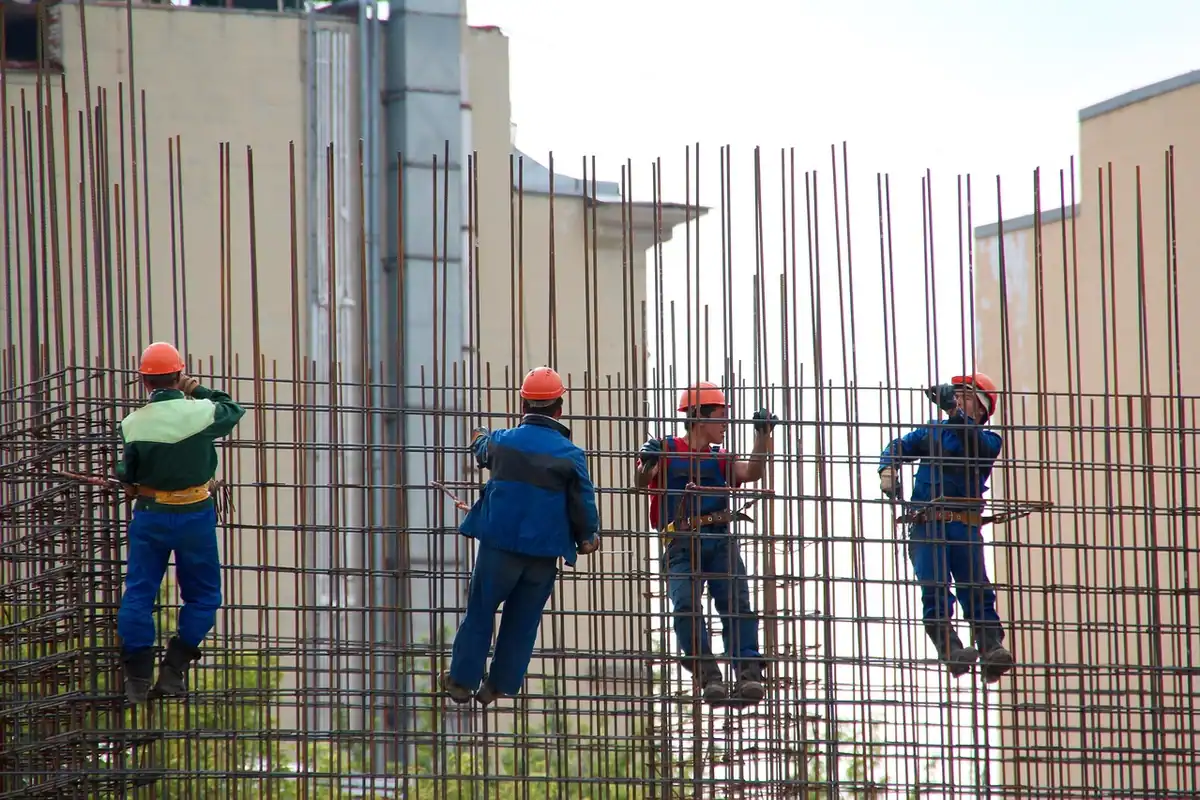 Muncitori cu căști oranj lucrează pe armătura unui perete de beton