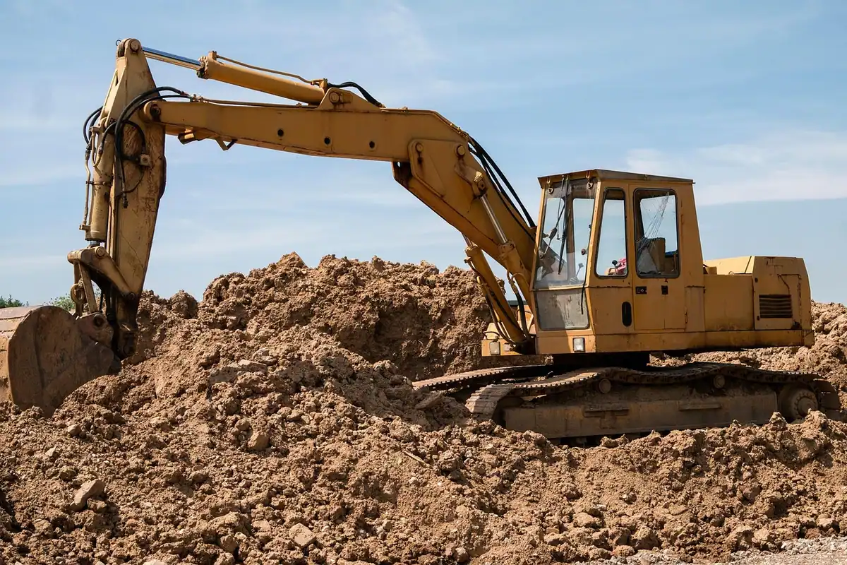 Excavator galben încarcă pământul dintr-un morman, sub cerul senin