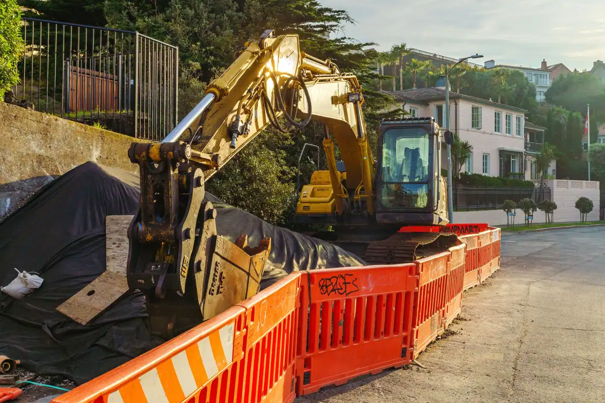 Excavator galben în spatele unor garduri oranj, pe un șantier urban