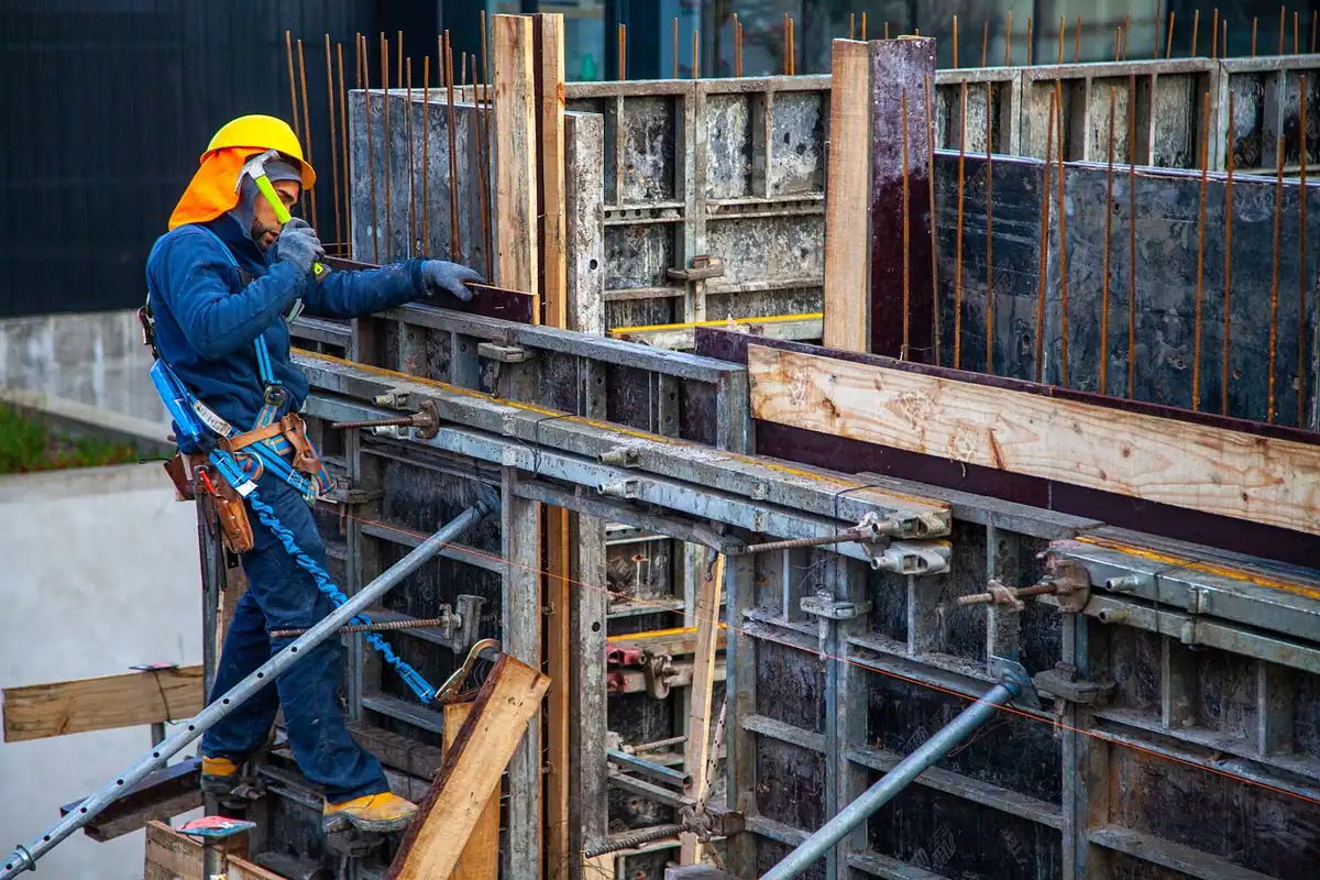 Muncitor cu cască fixează cofrajele de lemn la o structură de beton