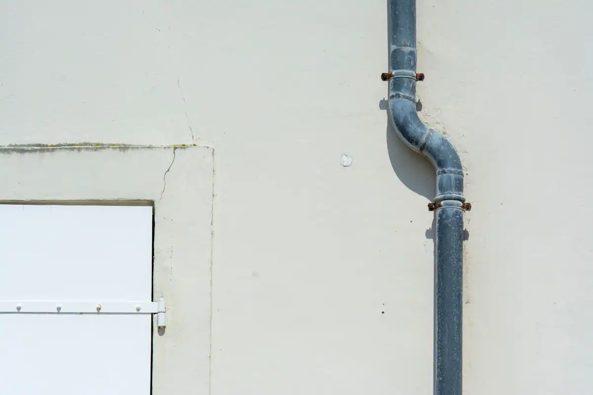 Prim-plan cu o țeavă de scurgere din metal gri fixată pe un perete exterior simplu