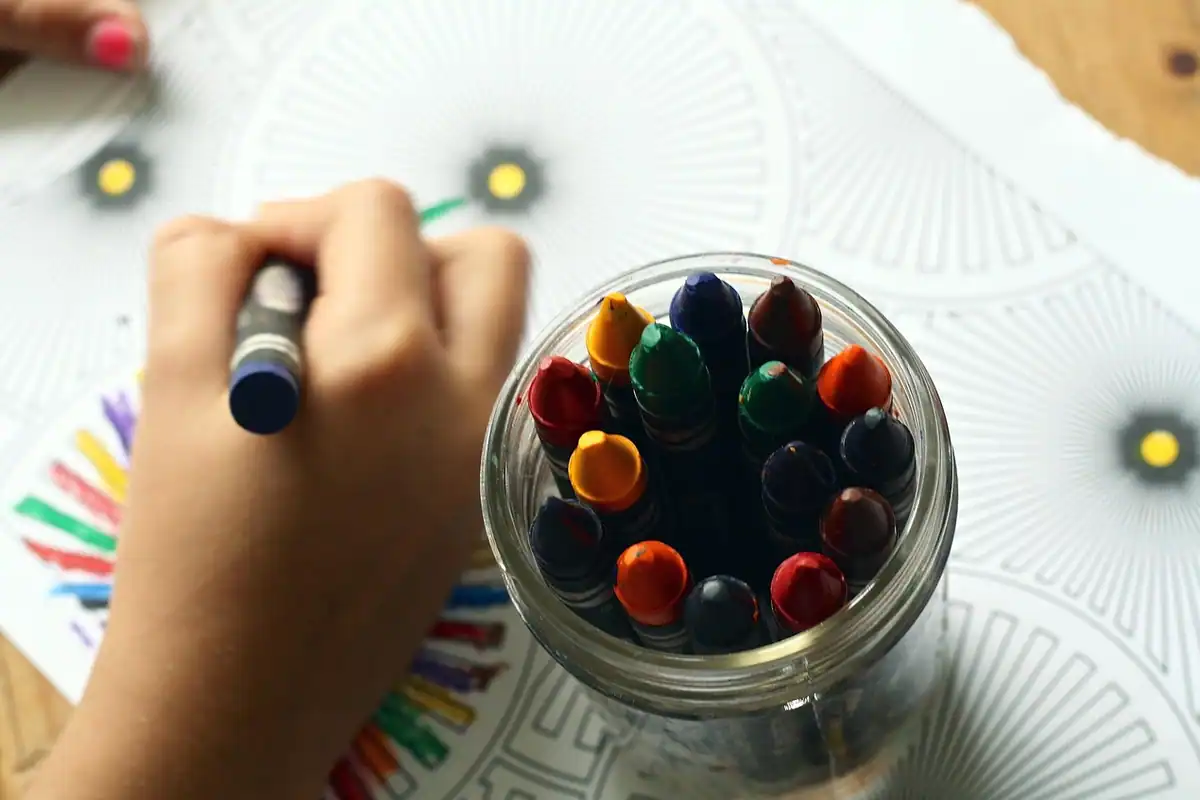 Creioane colorate și carte de colorat în mâna unui copil, cu materiale pentru desen